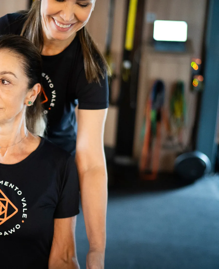 Professora corrige a postura de uma aluna durante um exercício com halter